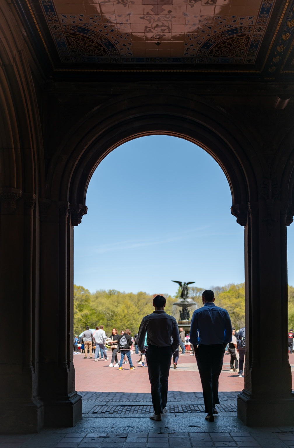 Two people walking through a shaded archway