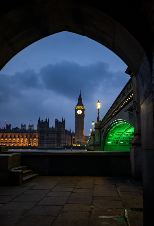 Big Ben and Westminster Bridge framed by a stone arch at dusk