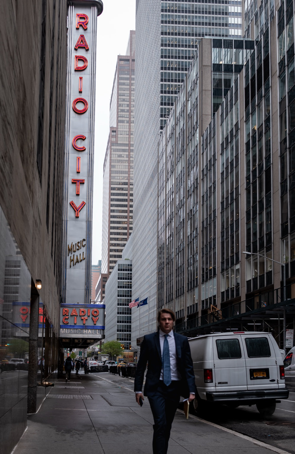 A man in a suit walking beneath the Radio City sign in New York